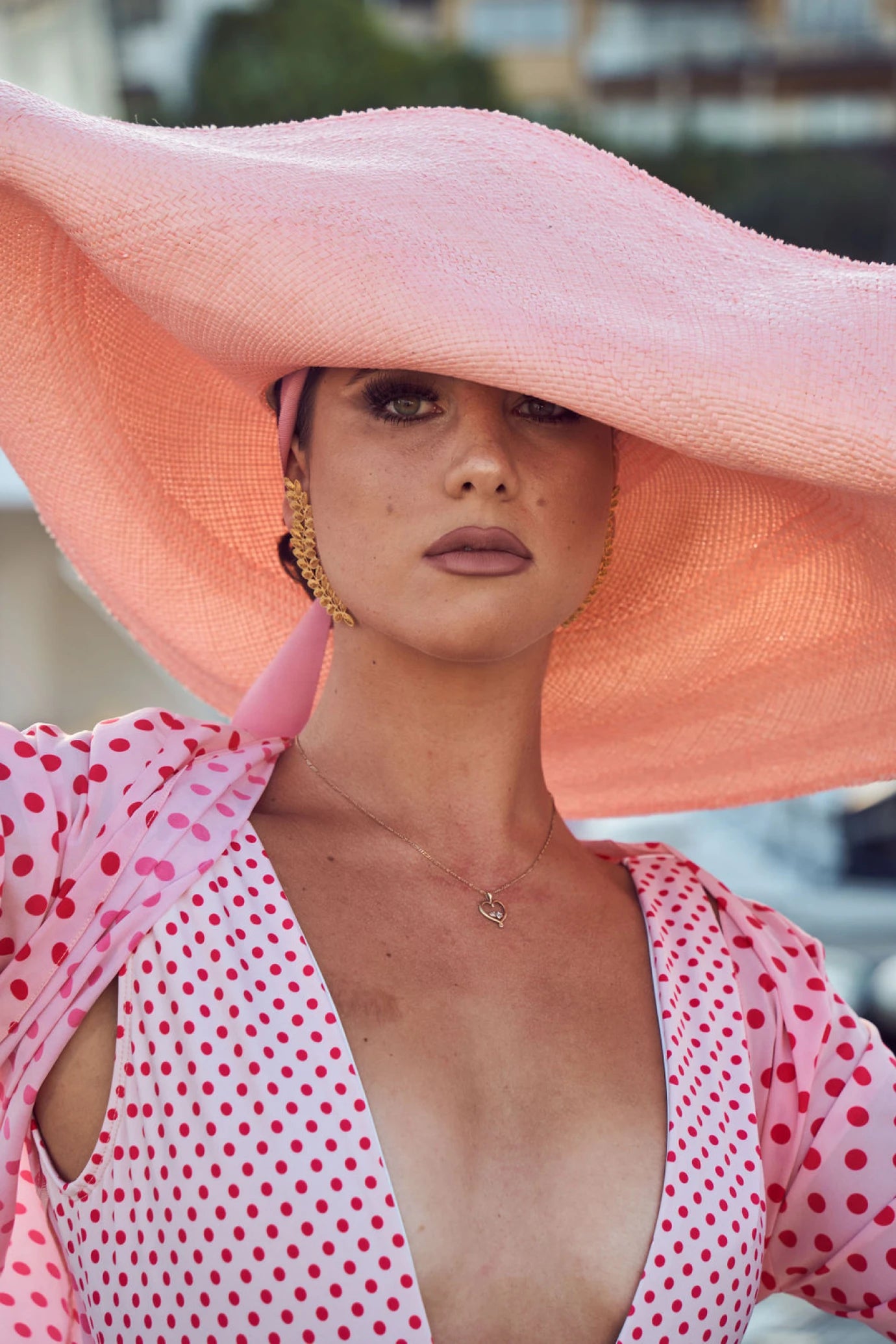 Close-up of model in the Lady Ibiza Hat with flowing ribbon ties, styled with gold accessories and a red polka dot dress—channeling retro Riviera elegance with a contemporary twist.