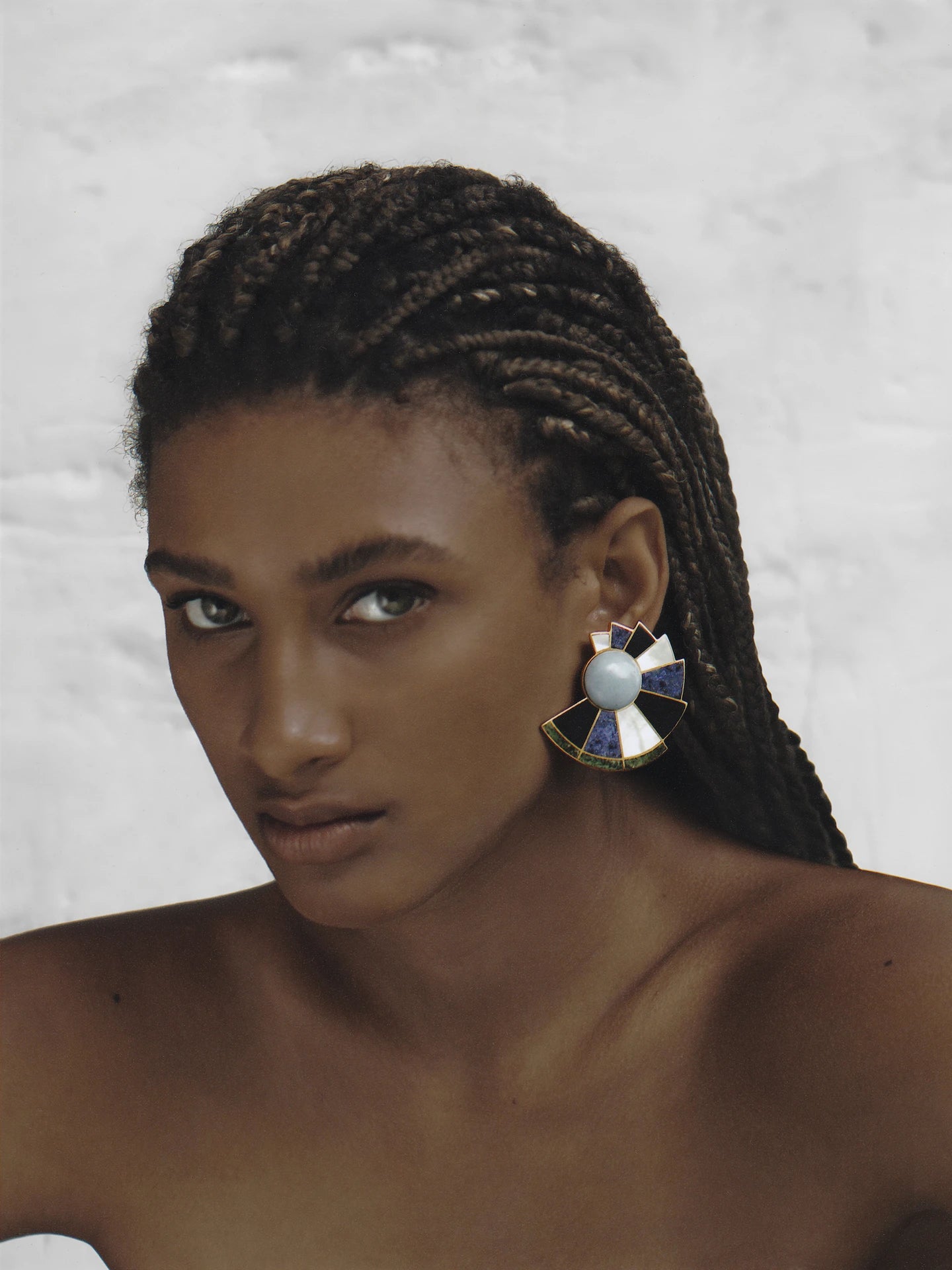 Model with braided hair wears bold multicolour stone earrings, styled with minimal makeup to highlight the intricate craftsmanship.