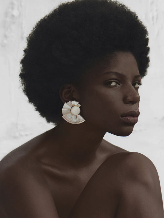 Stylish woman with natural hair wearing iridescent mother of pearl statement earrings with gold accents, adding a refined glow to her minimalist look.