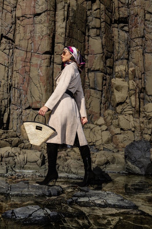 Model posed by a textured stone wall holding the Seashell Tote, showcasing its unique fan shape and elegant craftsmanship.