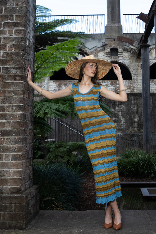 Model wearing the Paloma dress, standing confidently within a stone archway, showcasing the fitted silhouette and intricate knitted textures against a historic backdrop.