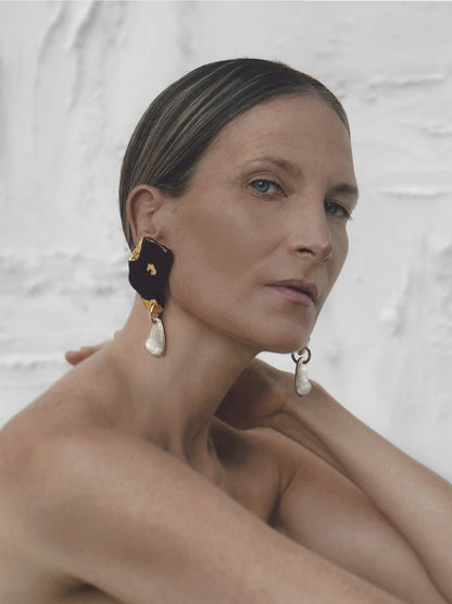 Elegant woman wearing sculptural black onyx and mother of pearl earrings, styled with a minimalist off-shoulder look to highlight the jewellery’s dramatic form.