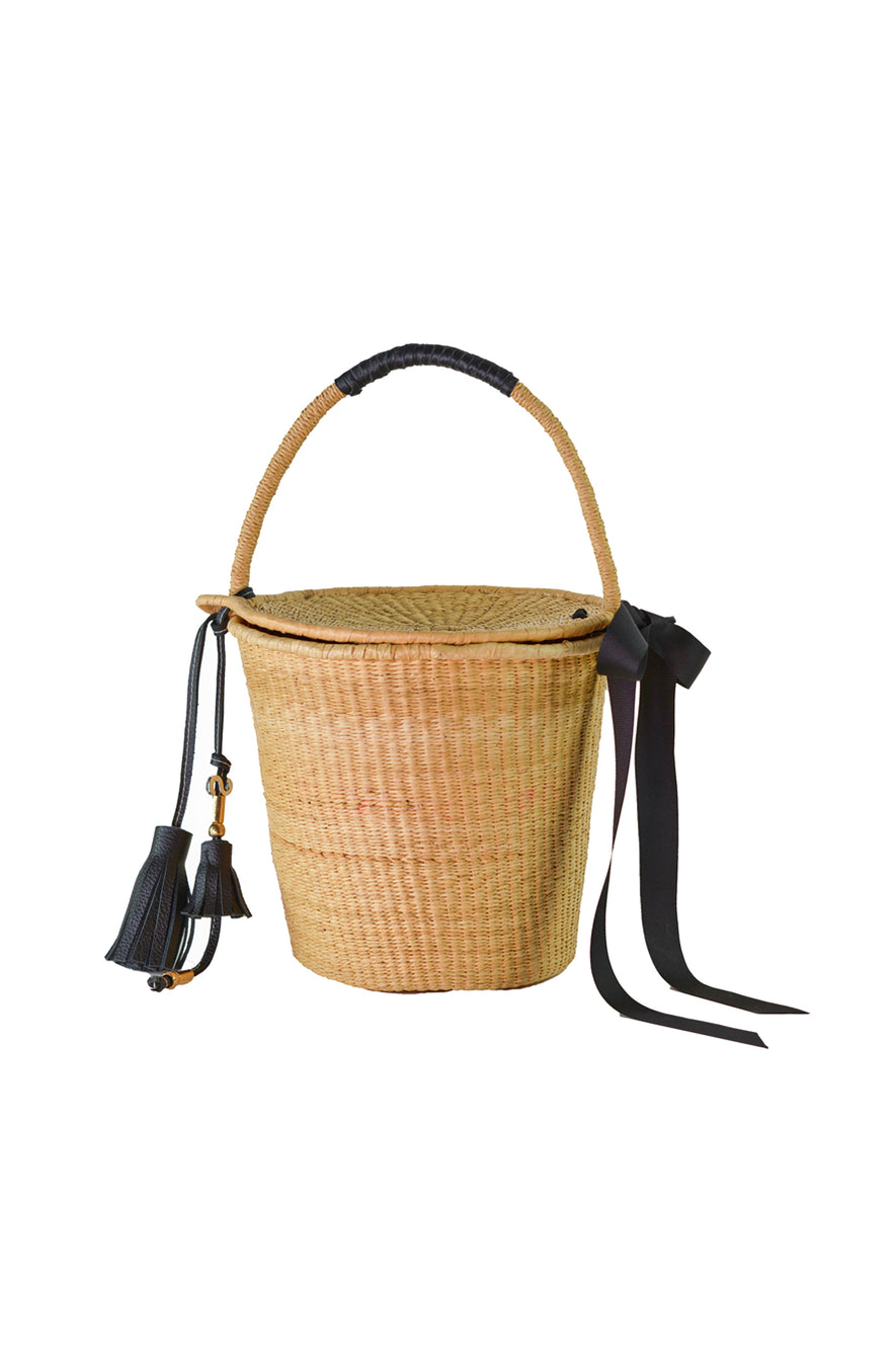 Handwoven natural basket bag with structured round base, black leather accents, long black bow detail, and tassel charm – inspired by classic Birkin style.