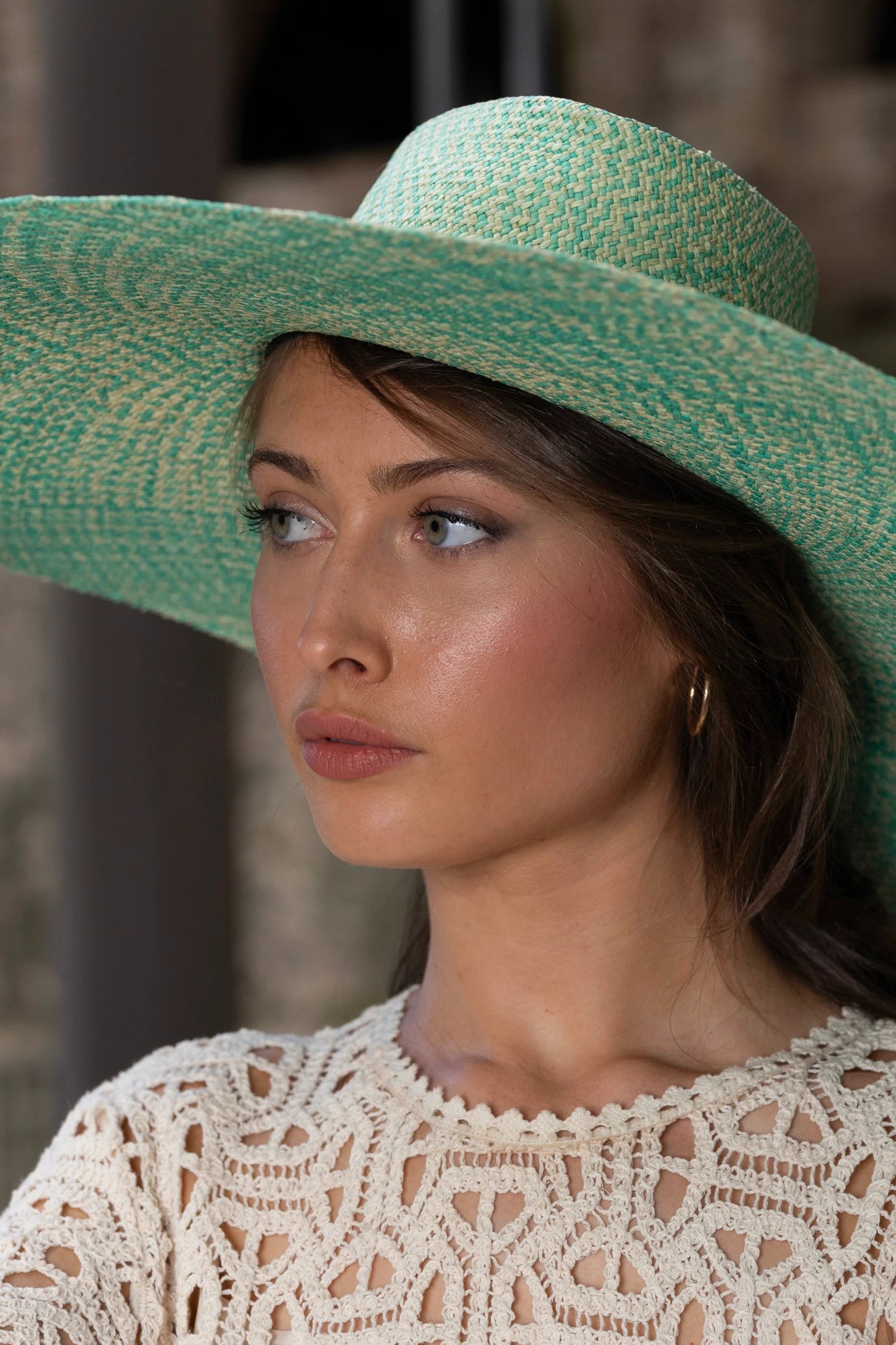 Close-up portrait of a model wearing the Chalan Sunhat in Surf Marino, highlighting the artisan weave in oceanic turquoise and sand tones, paired with a detailed ivory crochet top.