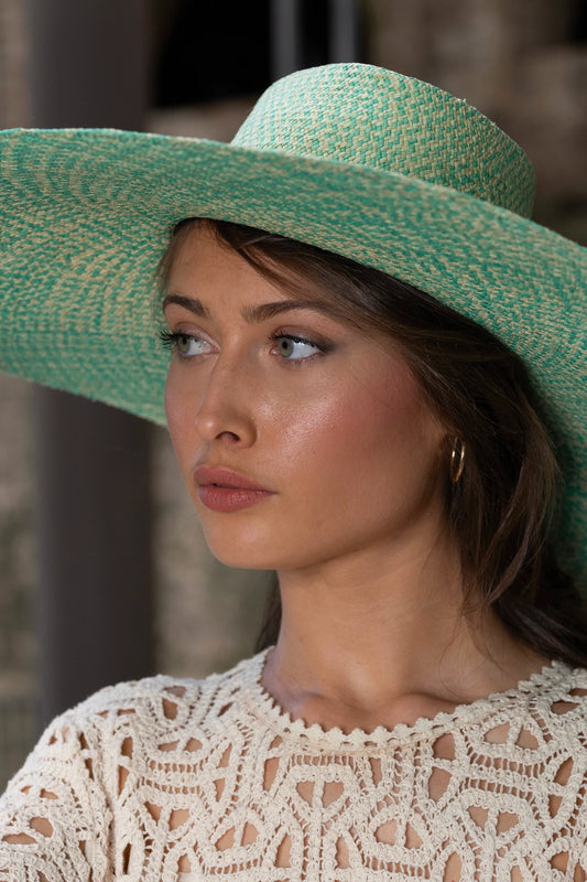 Close-up portrait of a model wearing the Chalan Sunhat in Surf Marino, highlighting the artisan weave in oceanic turquoise and sand tones, paired with a detailed ivory crochet top.