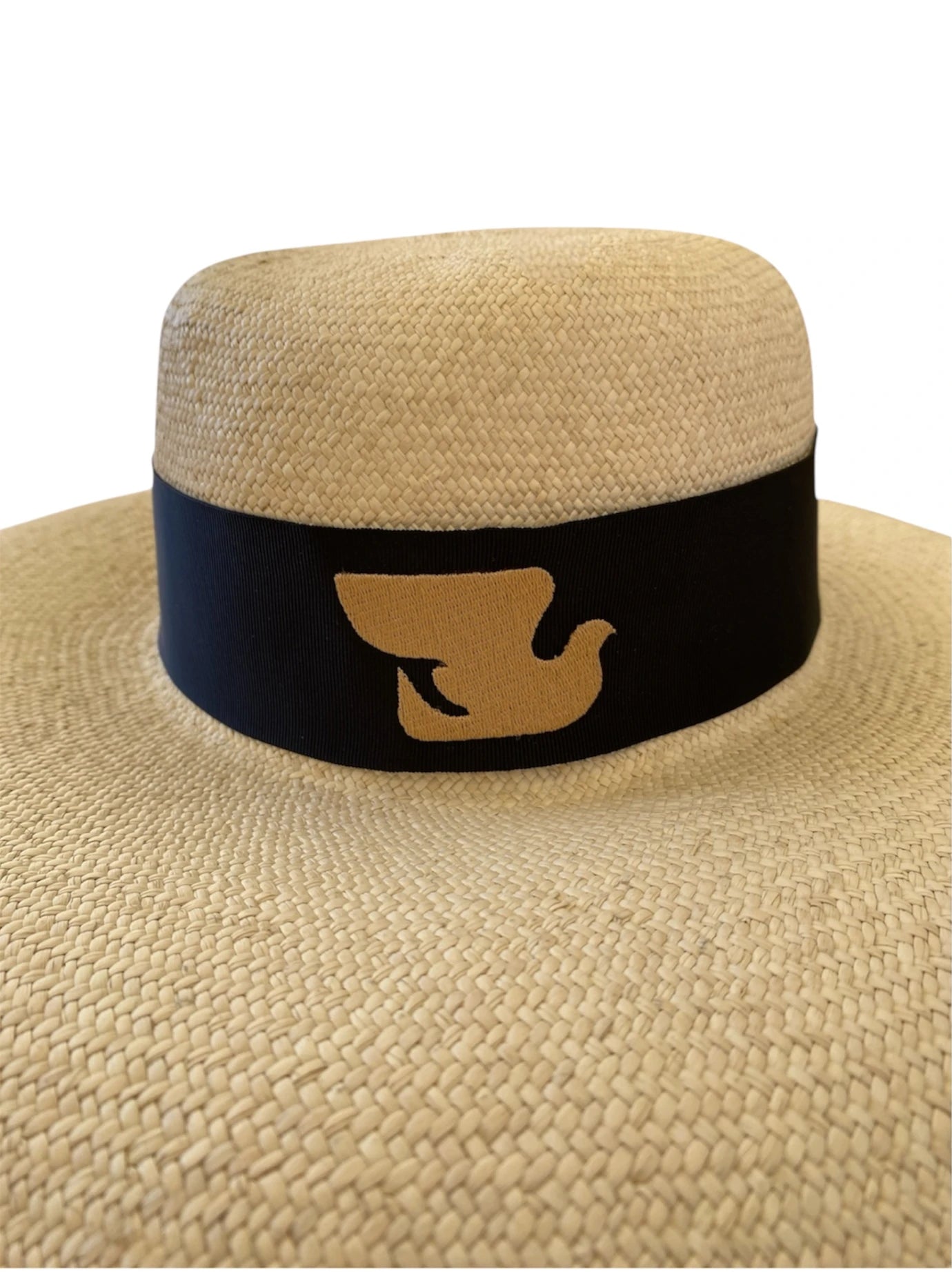 Close-up view of the Luna Hat’s crown and black ribbon, showcasing the embroidered gold dove emblem—symbolising the My Paloma brand’s refined minimalism and artisan heritage.