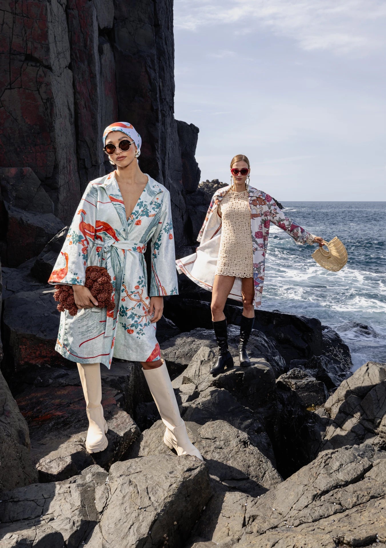 Two models on a rocky shore in Sydney, Australia wearing beautiful outerwear garments by My Paloma, featuring a trench coat and a kimono with bold prints. 
