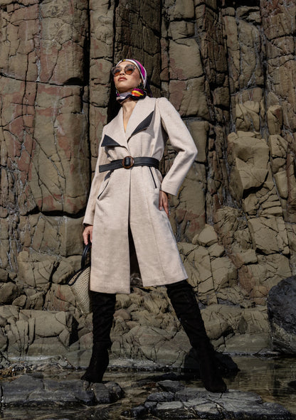
Girl wearing the Mia Belted Taupe Coat with wide lapels and black accents, captured in Madrid, Spain – timeless tailoring by My Paloma.  Paired with a straw bag and a silk head scarf on a rock shore