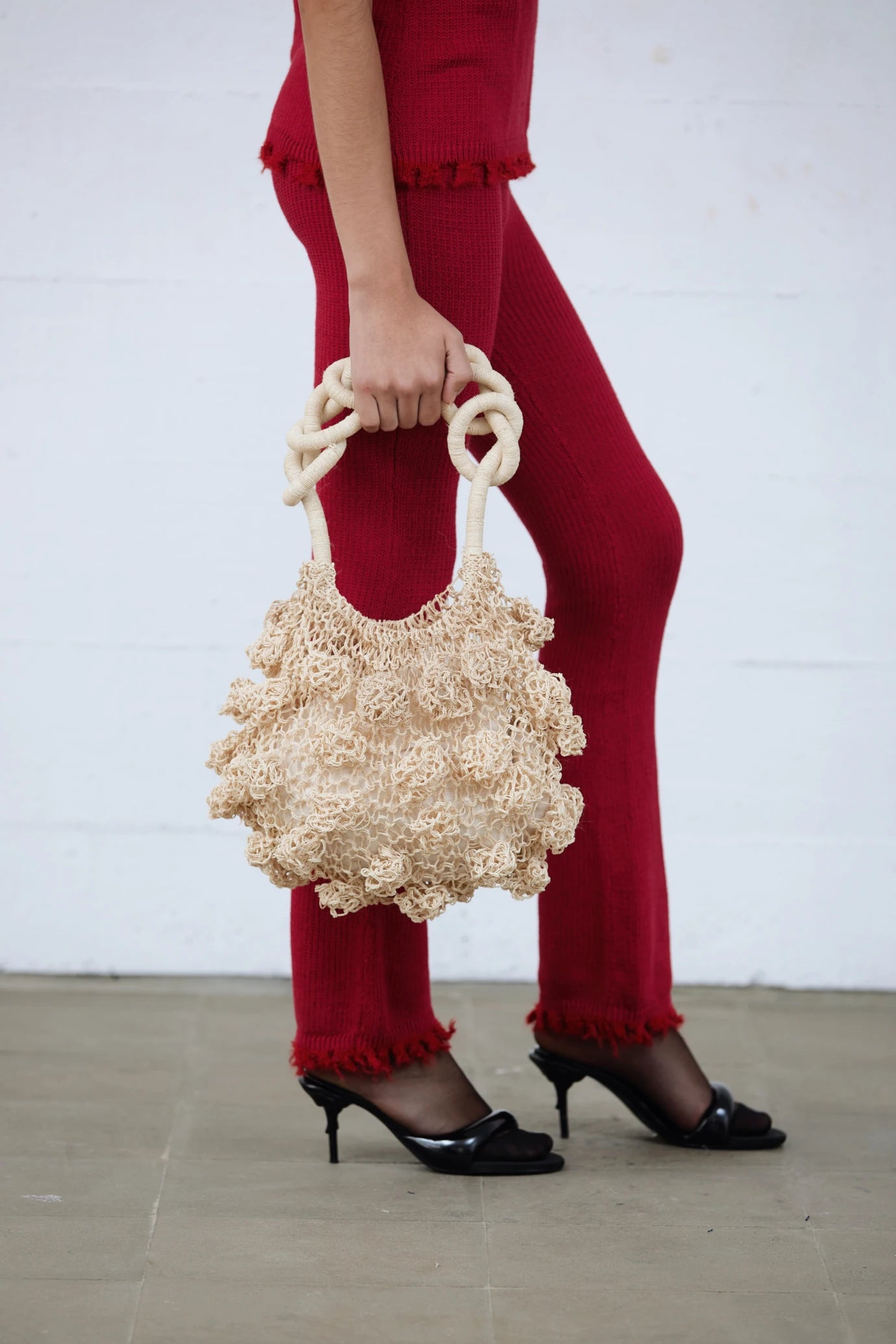 Cream Ameba Mesh Bag styled with bold red pants and heels, captured mid-stride in an urban location, Lima, Peru.