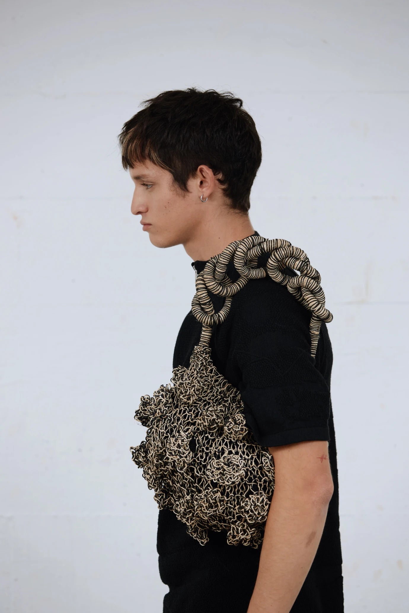 Male model in minimalist black tee holding the black Ameba Mesh Bag over shoulder, in a studio set-up inspired by Melbourne streetwear styling.