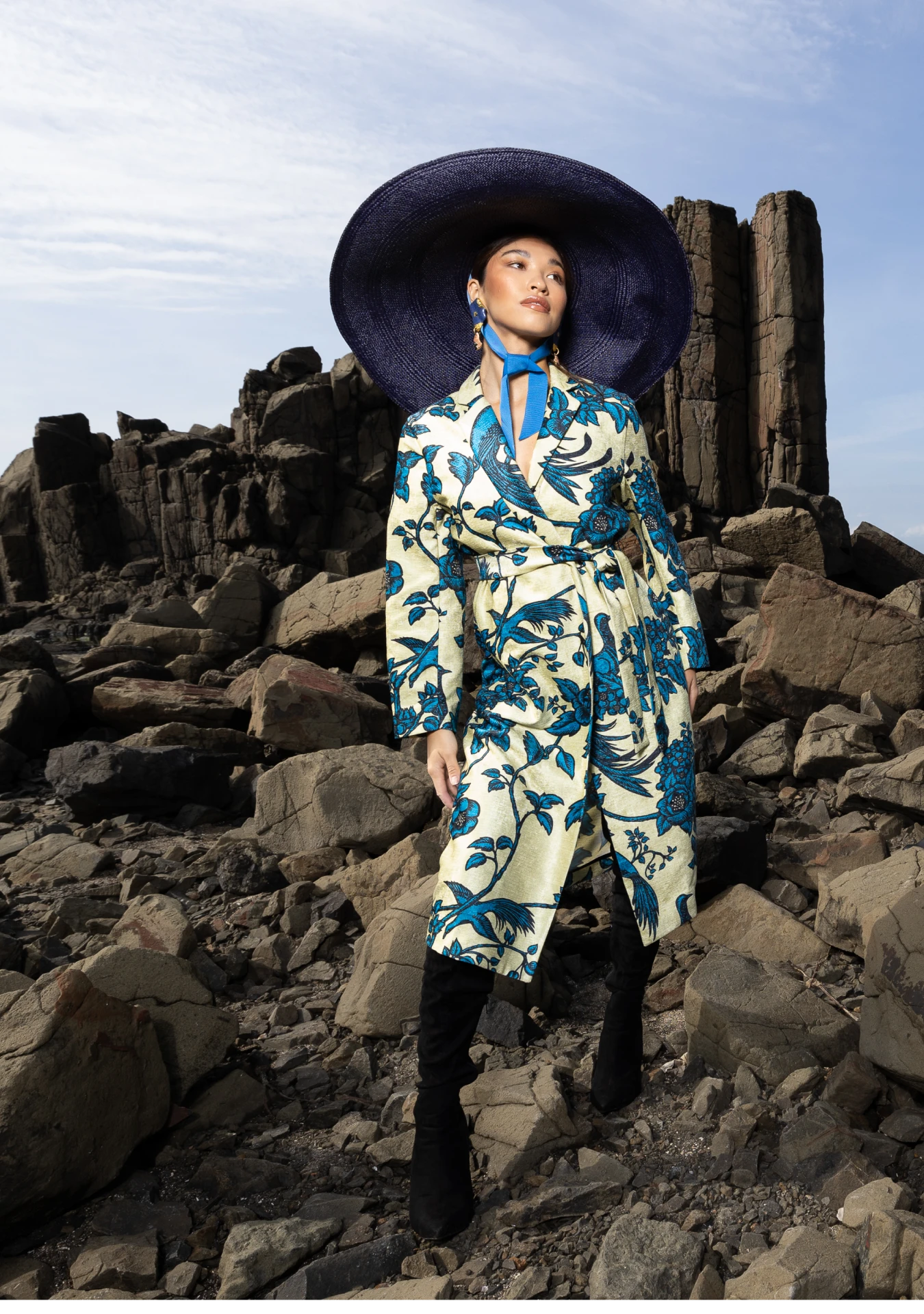 model wearing Birds of Paradise Coat with cinched waist and peacock print, captured in Los Angeles, California – My Paloma’s artistic approach to fashion. Model also wears thigh high boots and large brimmed hat.