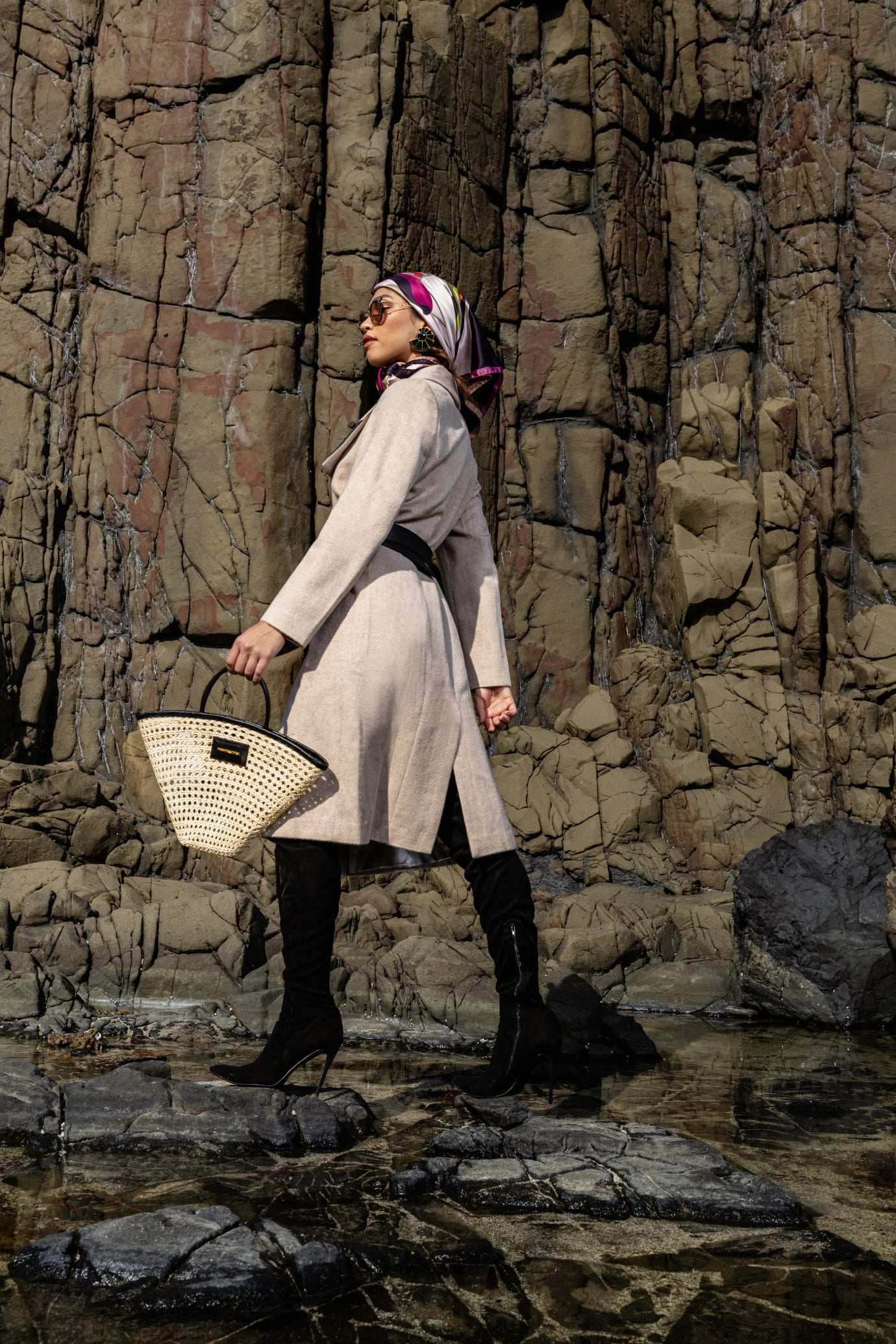 Model posed by a textured stone wall holding the Seashell Tote, showcasing its unique fan shape and elegant craftsmanship.