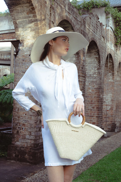 Model standing under soft daylight, styled in white attire and accessorising with the Verano Tote in hand, highlighting its artisanal weave and structured form.