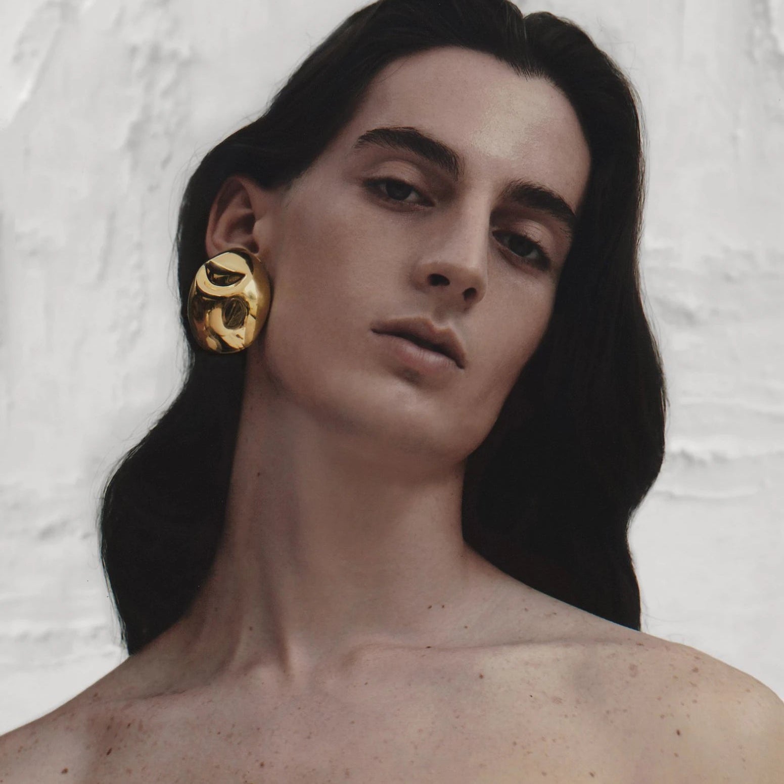 Profile shot of model with long dark hair showcasing statement gold sculptural earrings for a refined, gallery-inspired aesthetic.