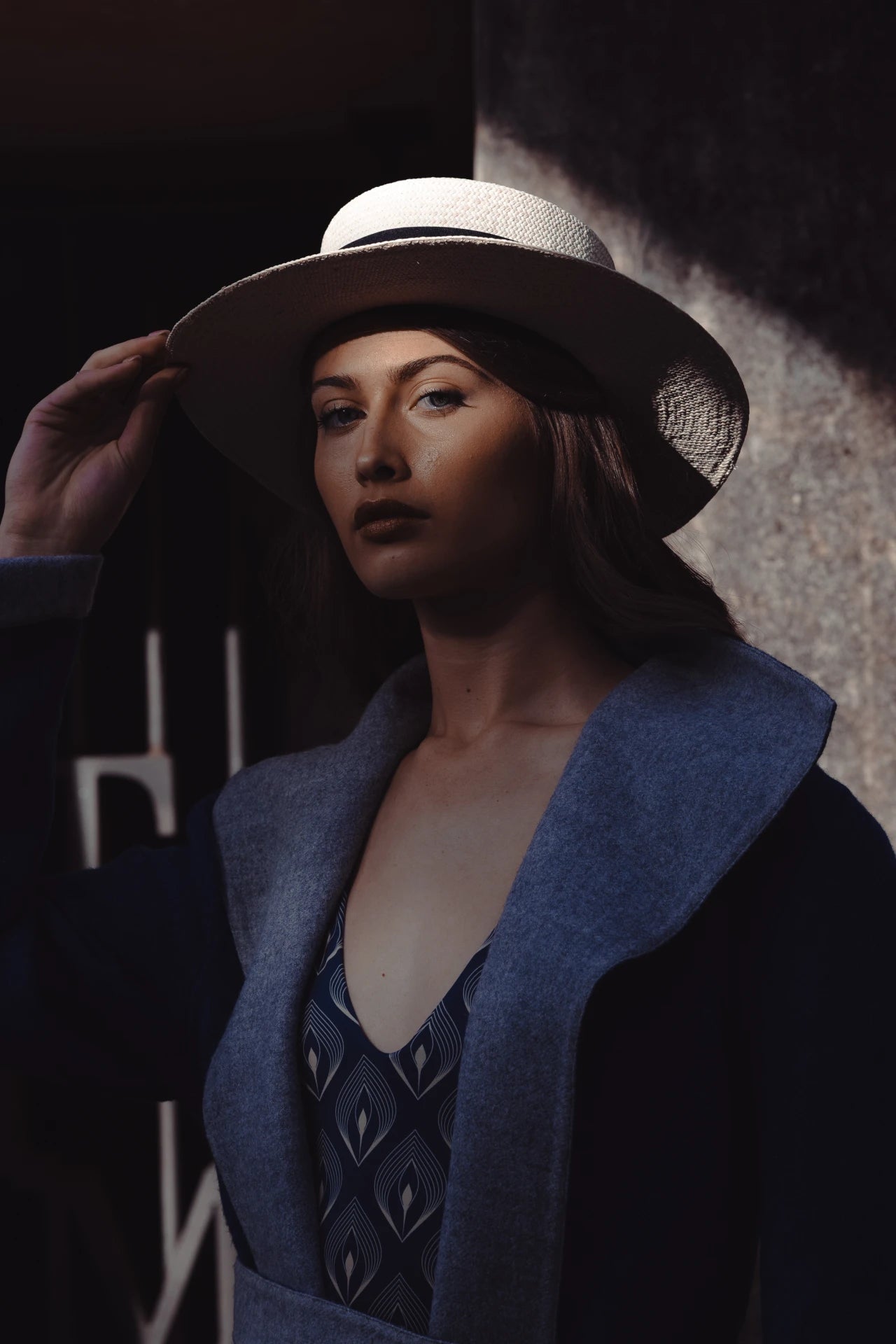 Dramatic shadowed portrait of model wearing the Wayra Hat, with sunlight catching the brim—creating a cinematic moment of elegance and intrigue.
