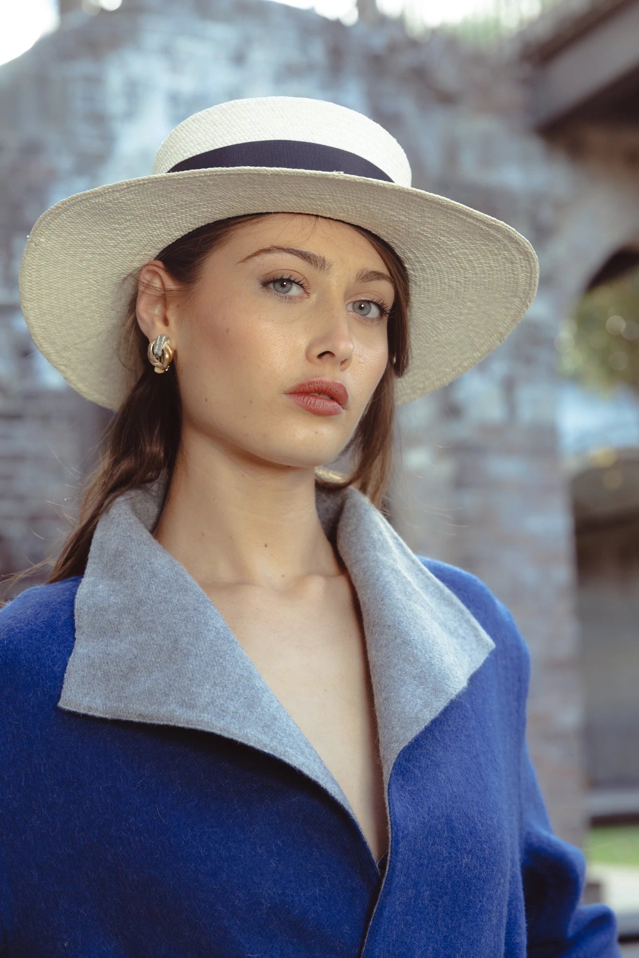 Close-up of model in the Wayra Hat outdoors, styled with a bold blue wool wrap coat and gold jewellery—merging European heritage style with contemporary minimalism.