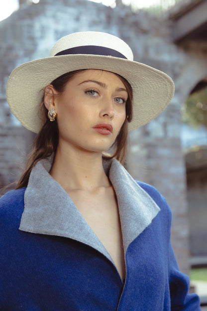 Close-up of model in the Wayra Hat outdoors, styled with a bold blue wool wrap coat and gold jewellery—merging European heritage style with contemporary minimalism.