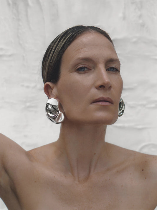 Minimalist model wearing silver sculptural earrings styled with slicked-back hair and bare shoulders for a refined, artistic profile.