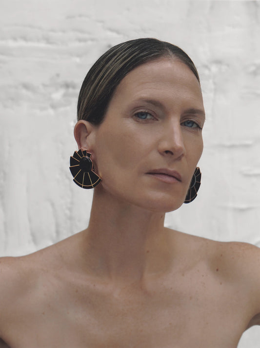 Elegant woman wearing structured black onyx fan earrings with gold trim, styled with an off-shoulder neckline for a dramatic statement.