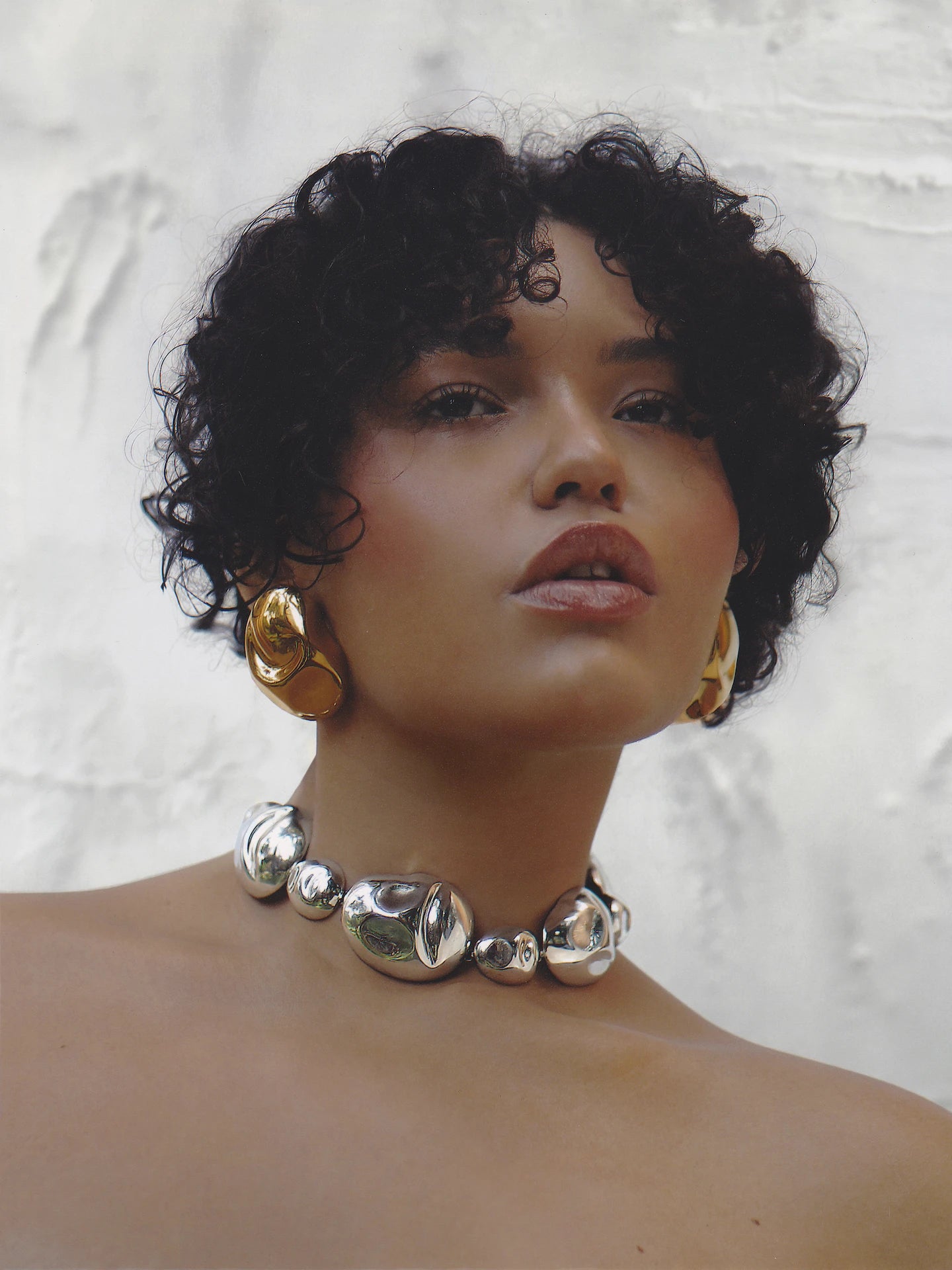 Curly-haired model styled in the bold silver necklace and earrings, exuding modern edge and luxury appeal.
