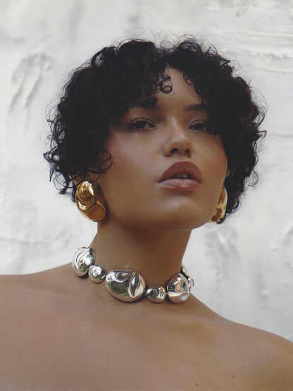 Curly-haired model styled in the bold silver necklace and earrings, exuding modern edge and luxury appeal.