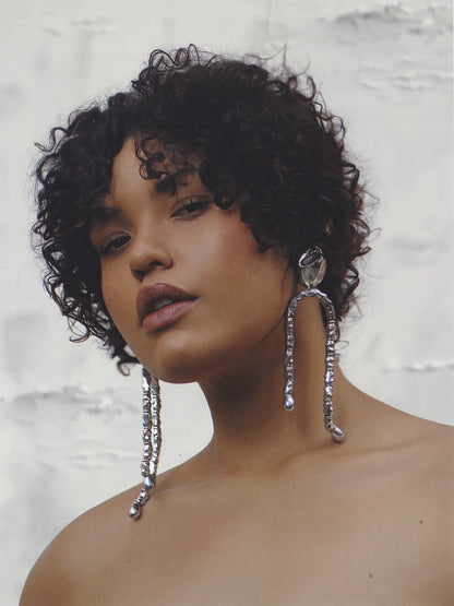 Close-up of a model with curly hair wearing long silver U-shaped drop earrings, highlighting their modern elegance and shoulder-grazing length.