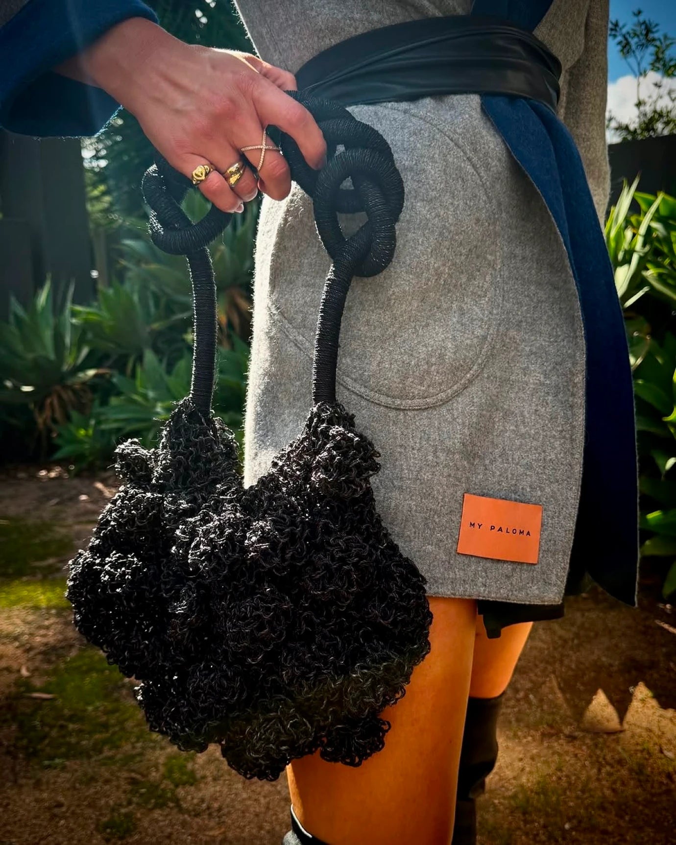 Model in blue printed dress holding the black Ameba Mesh Bag by the rocky cliffs of Lima’s coastline.